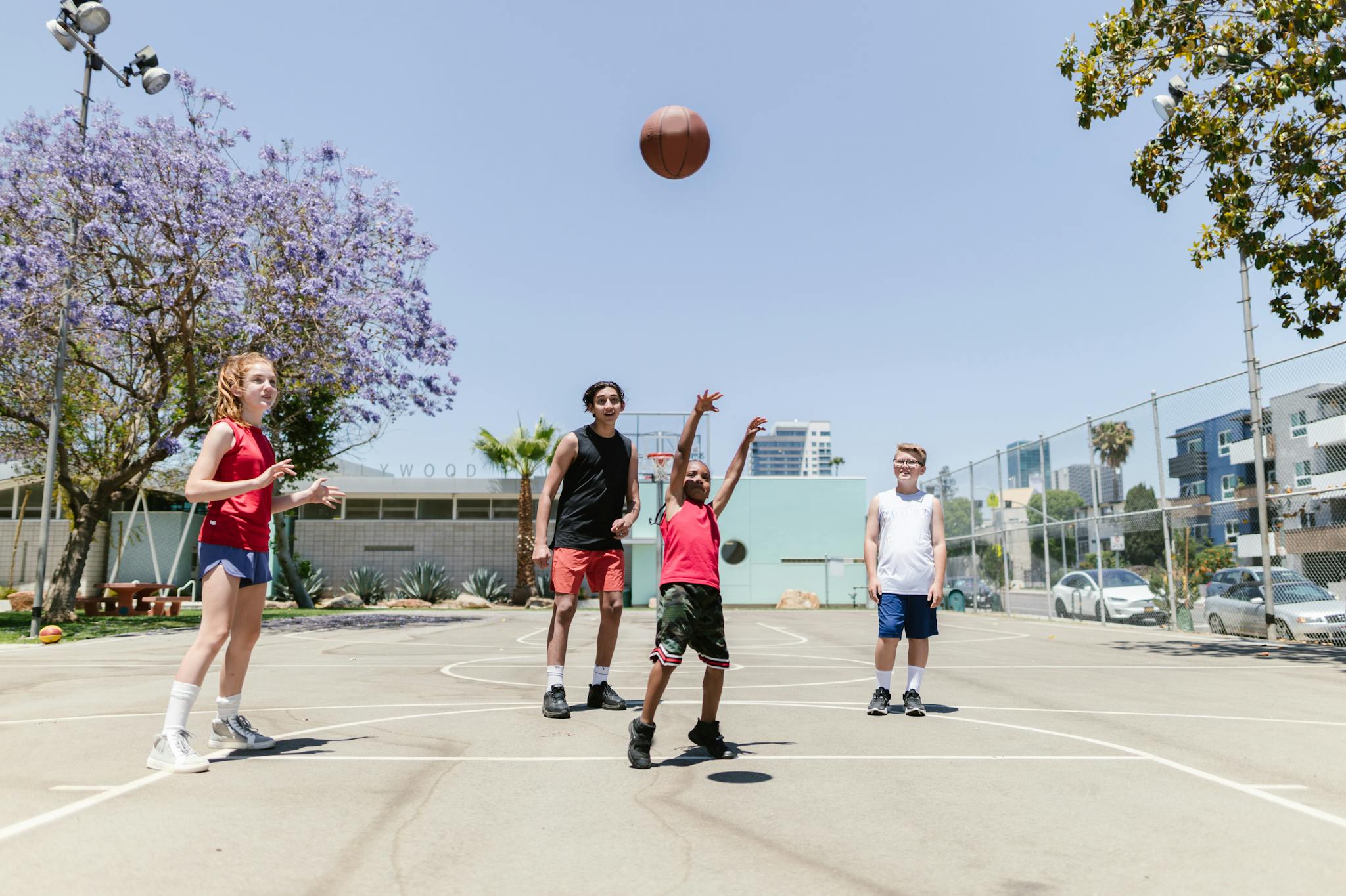 Diverse children playing basketball on an outdoor court during the day.